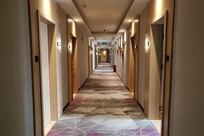 A hotel corridor with doors on both sides, a patterned carpet, and overhead lighting.