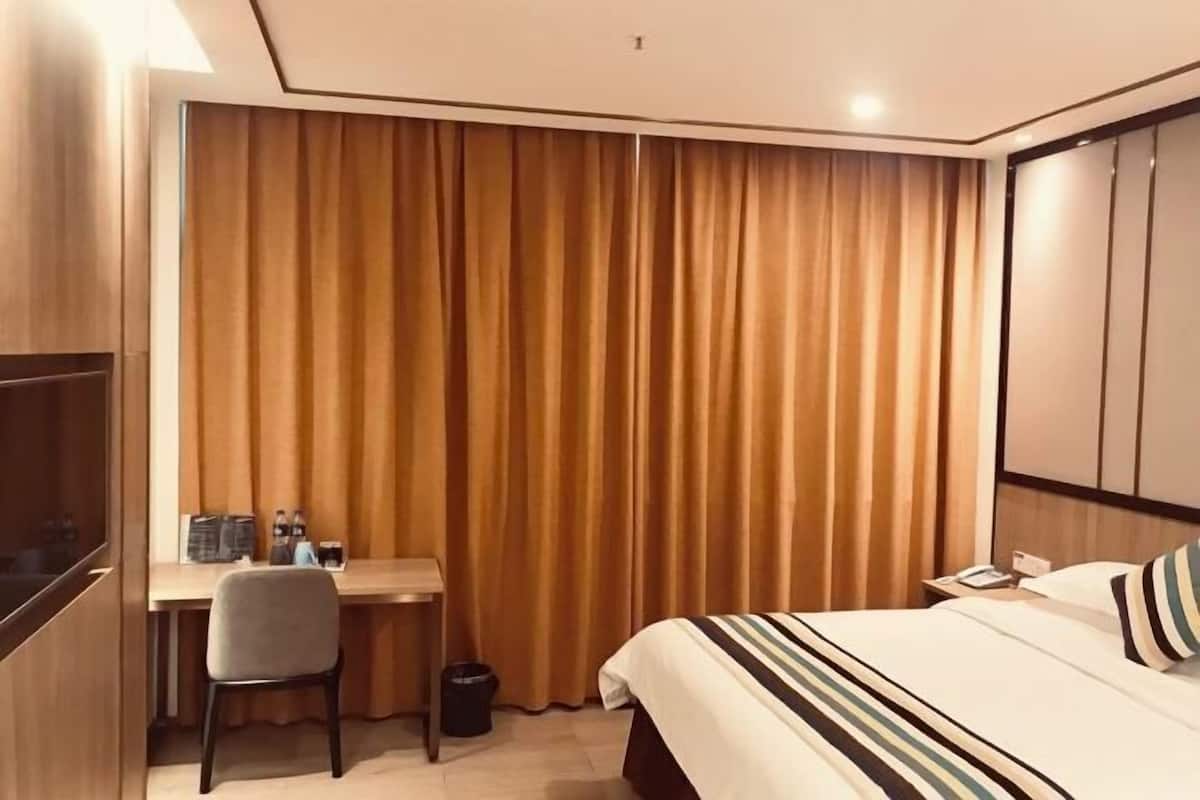 A hotel room with a bed, a desk, a chair, and a television.