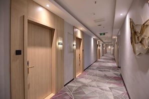Passadís d'hotel amb portes de fusta, alfàbega estampada i aplics de paret.