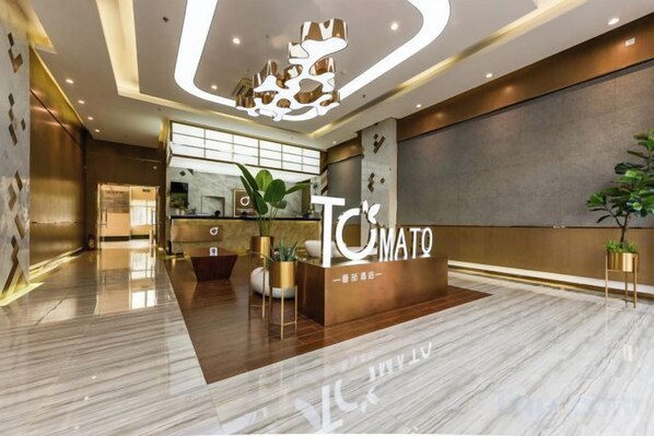 A hotel reception area with a reception desk, a large plant, and a modern chandelier.