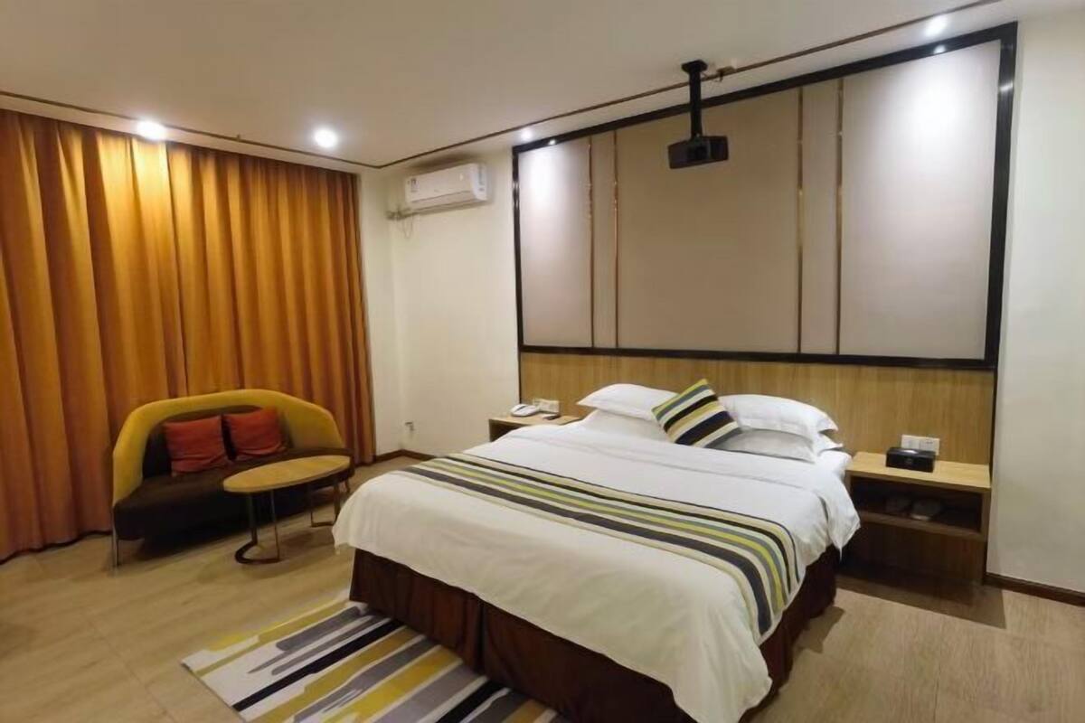 A hotel room with a bed, bedside tables, a sofa, a chair, a curtain, and a ceiling light fixture.