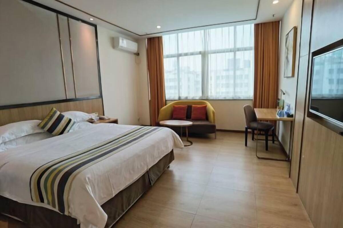 A hotel room with a bed, a small round table, a sofa, a TV, and a window with curtains.