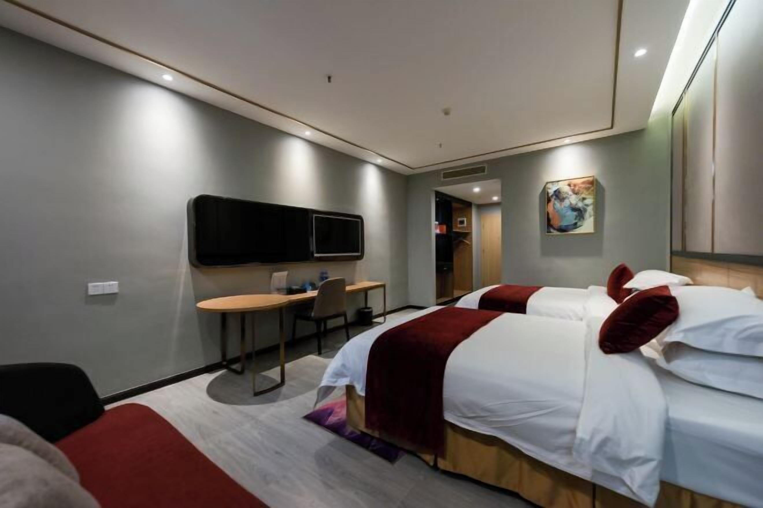 A hotel room with two beds, a desk, a chair, a flat-screen TV, and a painting on the wall.