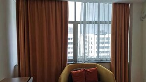 A room with a sofa, a small table, and a window with curtains. - Tomato Hotel (Dongguan)