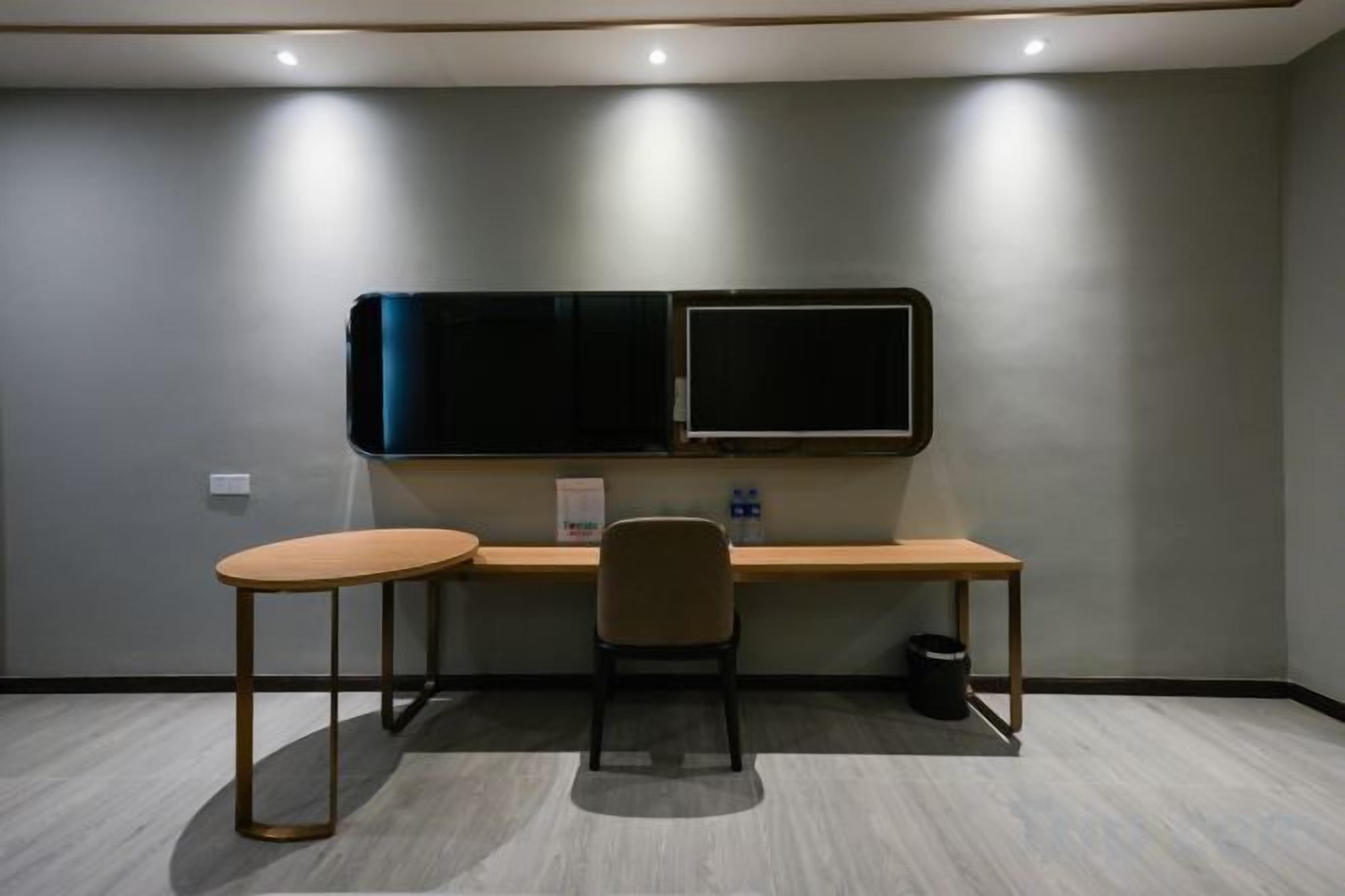 A room with a desk, two chairs, a television, and a trash can.