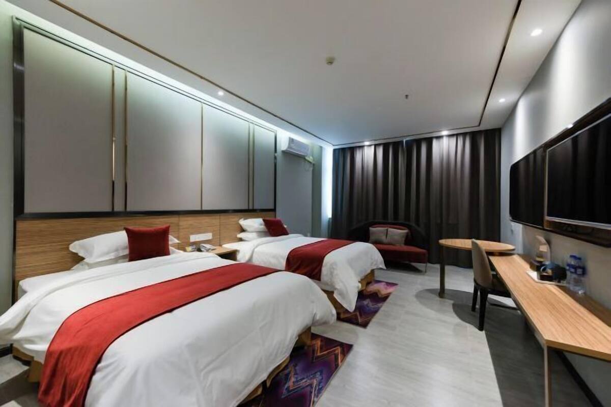 A modern hotel room with two beds, a desk, a chair, a TV, and a large wardrobe.