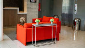 A modern hotel lobby with a red sofa, a small table with two potted plants, and a trash bin. - Royal Delonix Hotel (Penuelas)