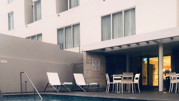 A swimming pool with lounge chairs and a table, surrounded by a building with multiple windows and a door leading inside. - Royal Delonix Hotel (Penuelas)