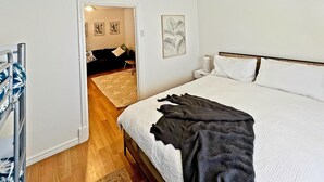 Un dormitorio con cama, ventilador de techo, mesita de noche y una puerta que da a otra habitación.