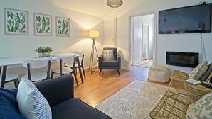 A modern living room with a sofa, a dining table with chairs, a floor lamp, a television, and framed artwork on the wall. - Sea Salt Apartment 3 - Short walk to beach! Free WiFi! newly decorated! (Stansbury)
