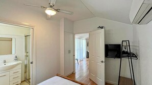 A bedroom with a bed, a bathroom with a sink, a ceiling fan, and a TV on a stand. - Sea Salt Apartment 3 - Short walk to beach! Free WiFi! newly decorated! (Stansbury)
