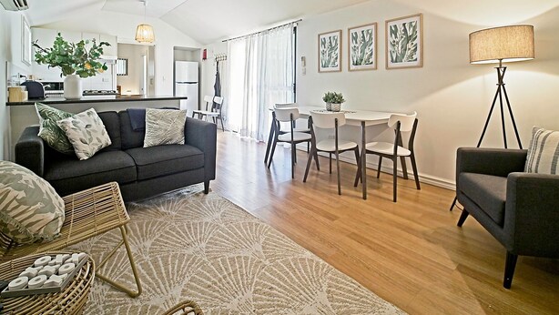 A modern living room with a dark sofa, a dining area with a white table and chairs, and a kitchen in the background. - Sea Salt Apartment 3 - Short walk to beach! Free WiFi! newly decorated! (Stansbury)