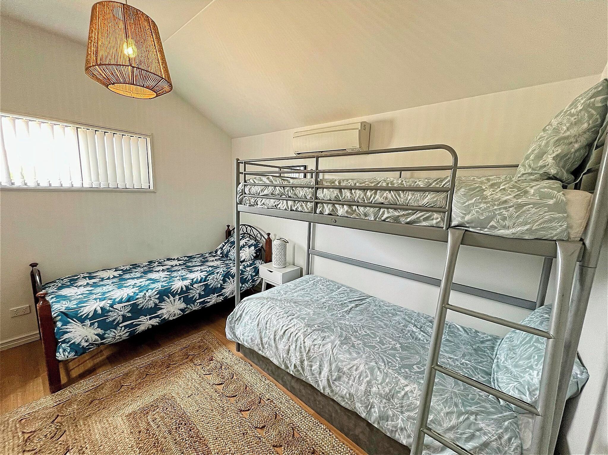 A bunk bed room with a window, a bedside table, and a hanging light fixture.