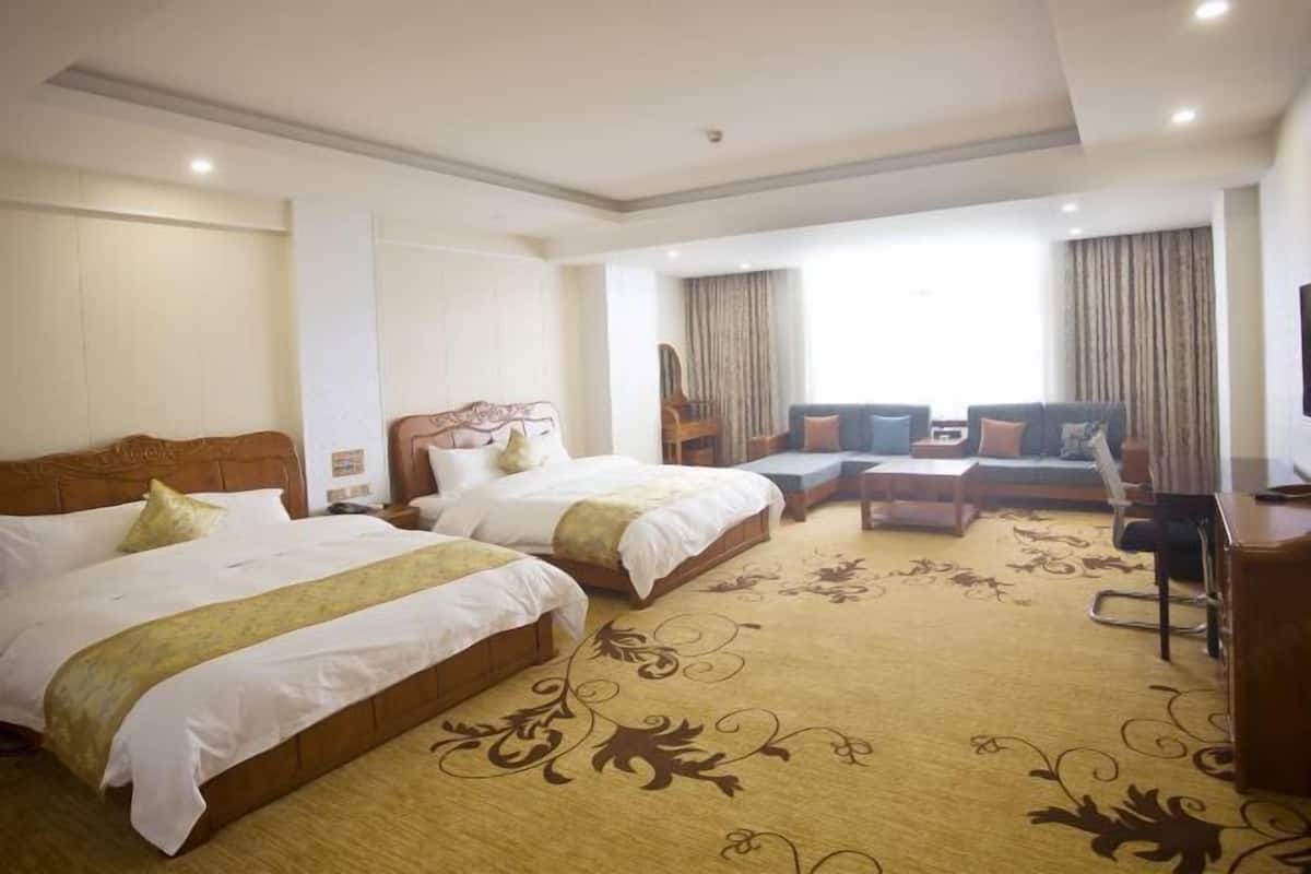 A hotel room with two beds, a sofa set, a desk, and a large window with curtains.