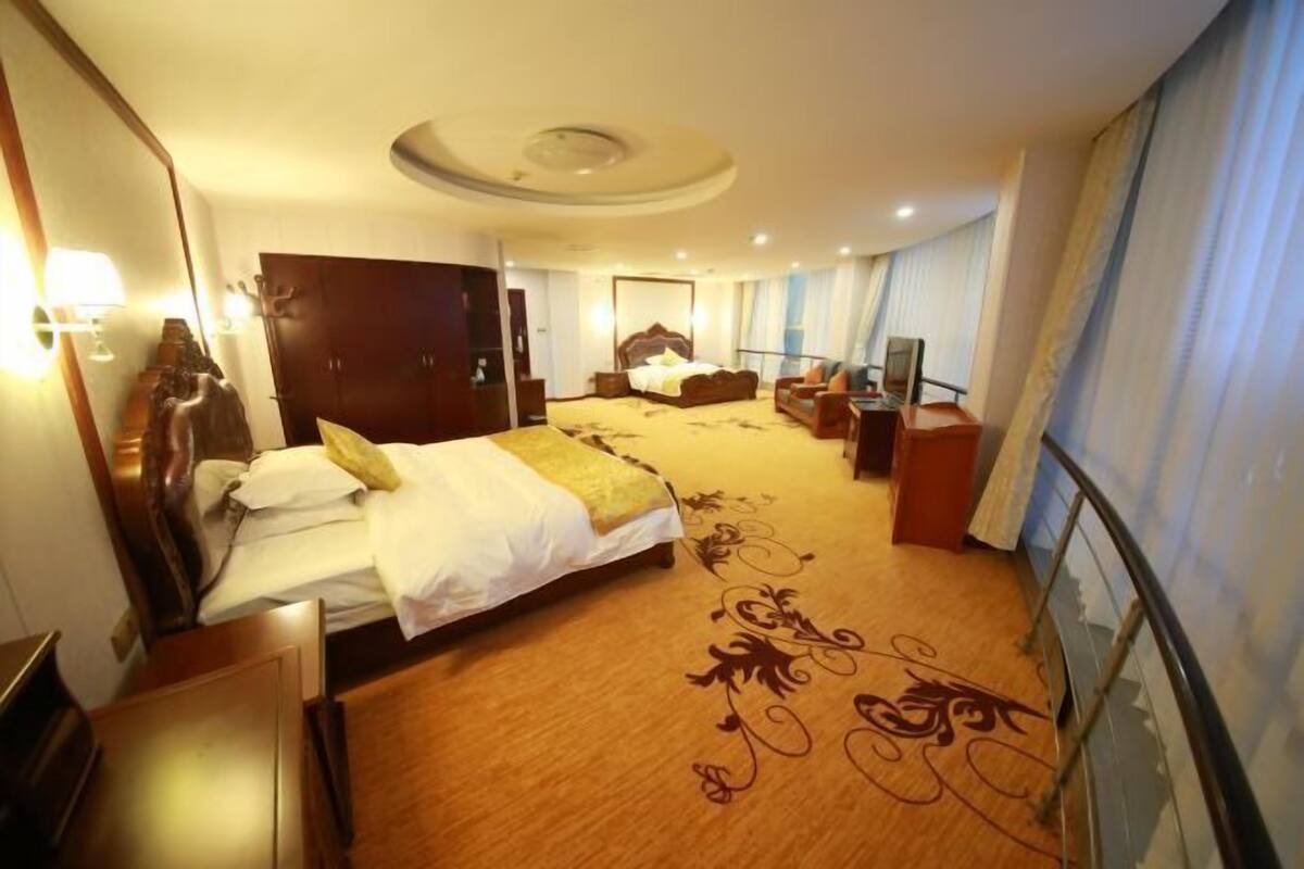 A hotel room with a large bed, a desk, a chair, a TV, and a wardrobe.