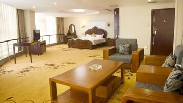 A hotel room with a bed, a sofa, a wooden coffee table, a TV, and a large window with curtains.