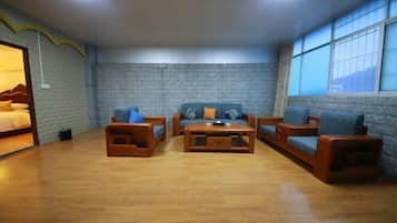 Une pièce avec un mur en briques, un plancher en bois et une grande fenêtre. On y trouve un lit avec une tête de lit, un ensemble de canapés avec des coussins et une table basse.