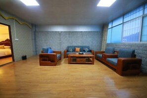 Une pièce avec un mur en briques, un plancher en bois et une grande fenêtre. On y trouve un lit avec une tête de lit, un ensemble de canapés avec des coussins et une table basse.