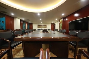 A conference room with a long table and multiple chairs, equipped with a projector and a large screen. - Family Portrait Grand Hotel (Guidong)
