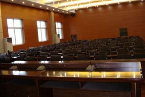 A conference room with rows of chairs, a long table with microphones, and large windows. - Family Portrait Grand Hotel (Guidong)