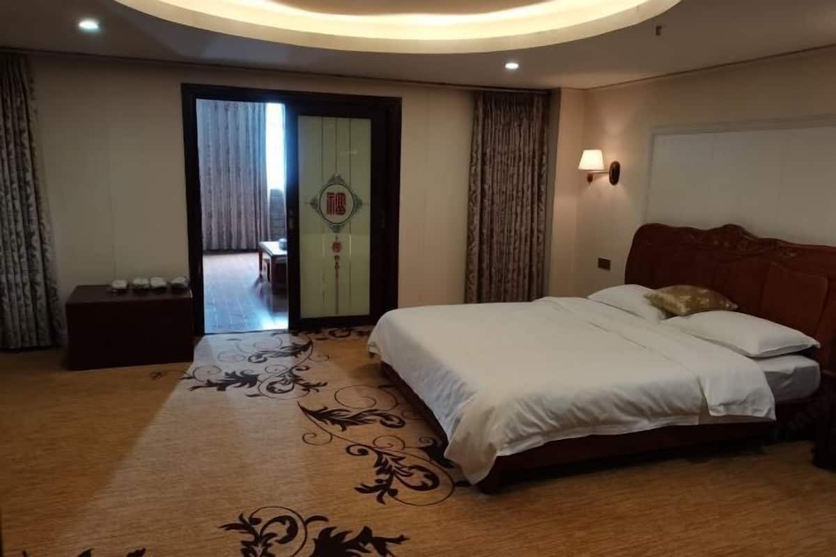 A hotel room with a large bed, a small bedside table, a wall-mounted lamp, and a door leading to a balcony.