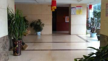 Un hall de hotel con piso de mármol, plantas en macetas y una puerta roja.