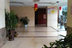 Un hall de hotel con piso de mármol, plantas en macetas y una puerta roja.