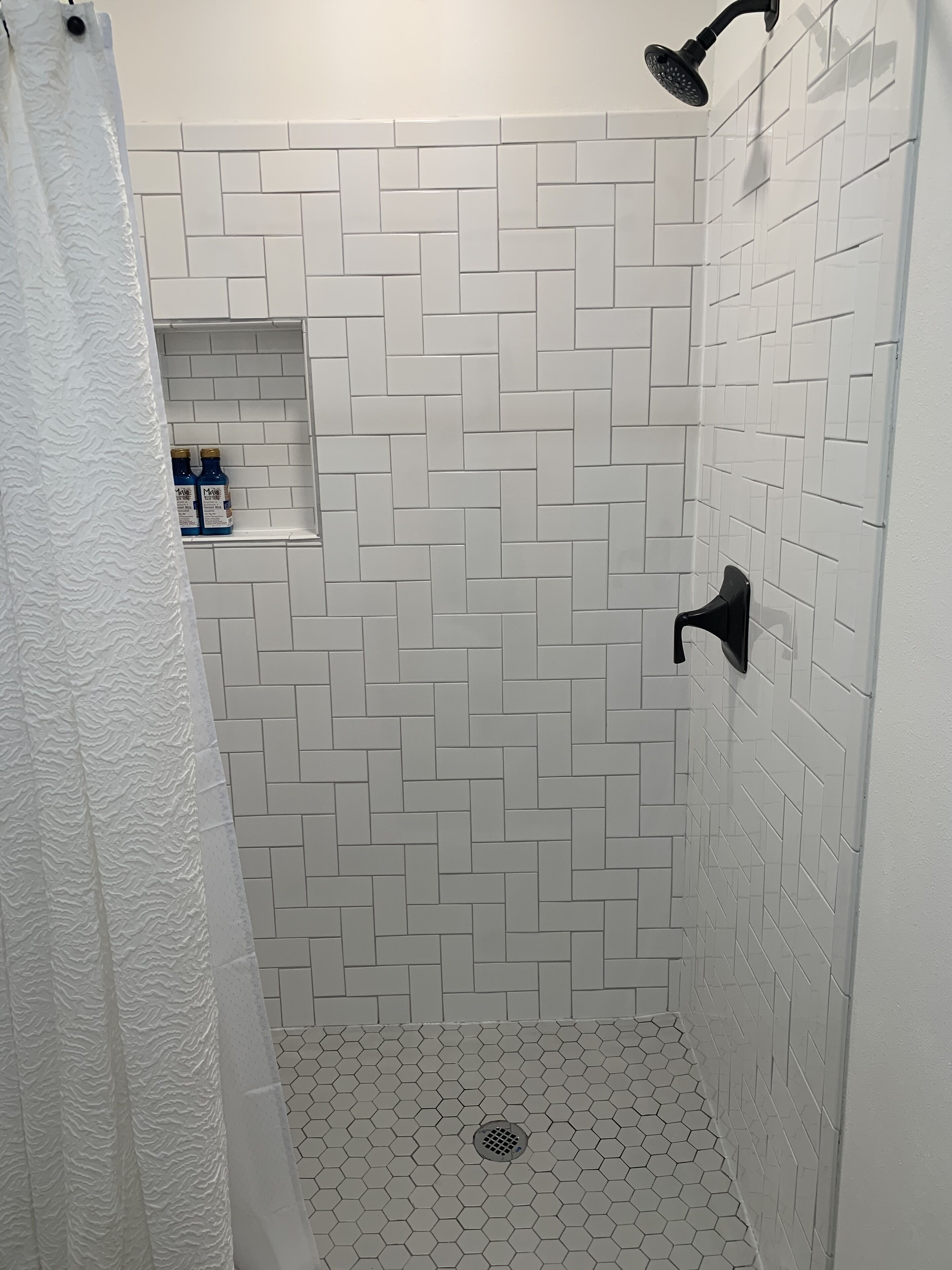A shower with a white herringbone tile pattern and a hexagonal tile floor.