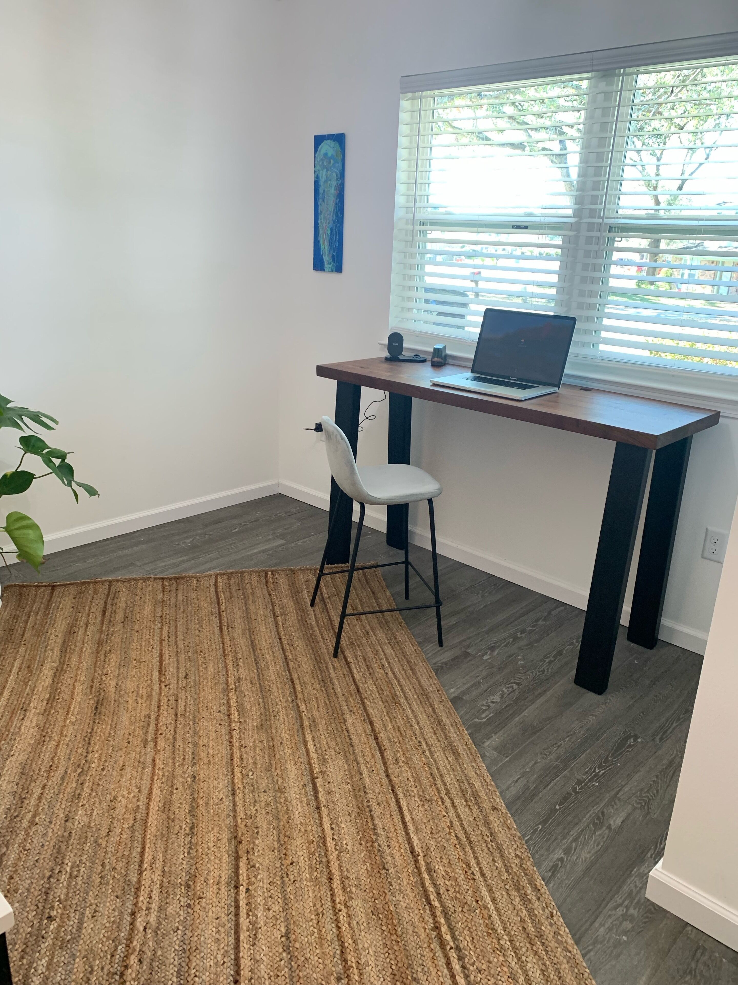 A workspace with a desk, chair, laptop, and a window with blinds.