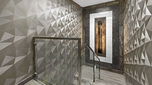 A modern interior with geometric patterned walls, a glass railing, and a view of a room with a wooden door. - Casa Azul Hotel Blu JFK (Queens Village)
