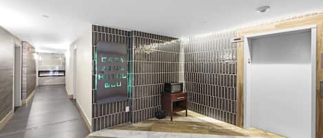 A hotel hallway with a modern design, featuring a wooden floor, tiled walls, and a neon sign.