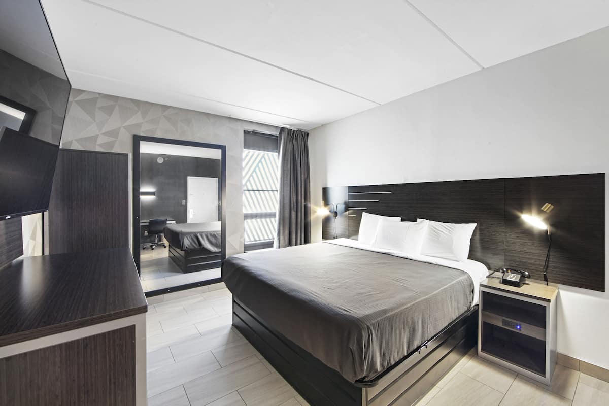 A modern hotel room with a large bed, bedside table, and a TV.