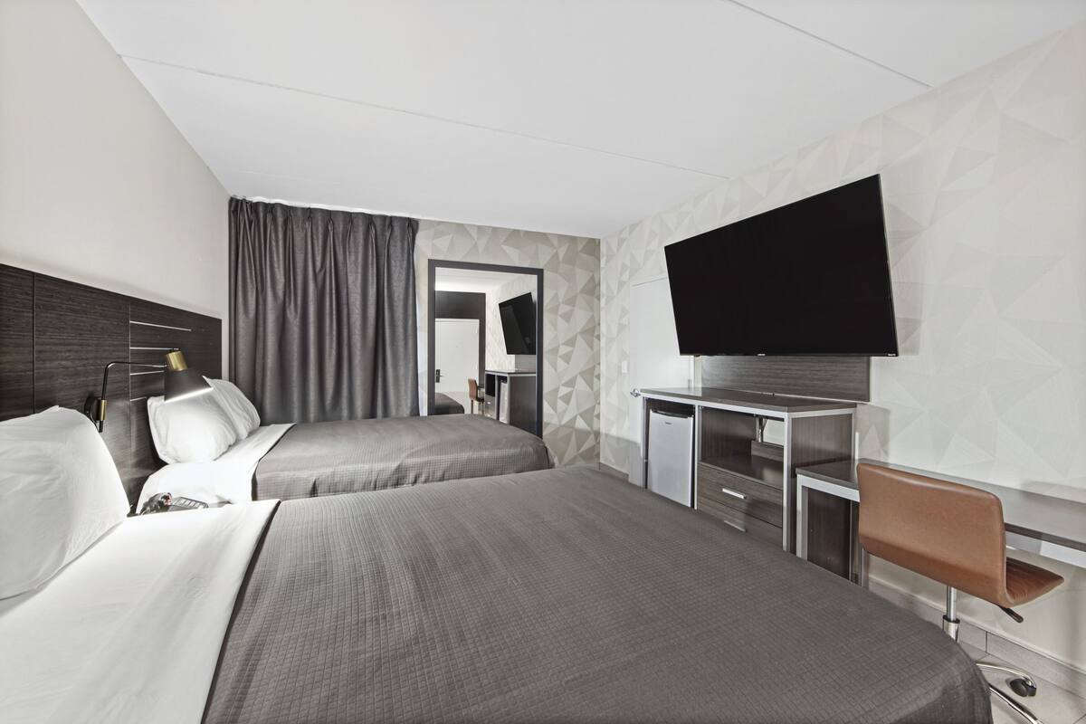 A hotel room with two beds, a desk, a chair, a flat-screen TV, and a mirror.
