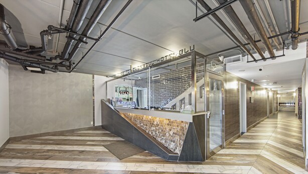 A hotel reception area with a modern design, featuring a reception desk, a staircase, and a herringbone-patterned floor. - Casa Azul Hotel Blu JFK (Queens Village)