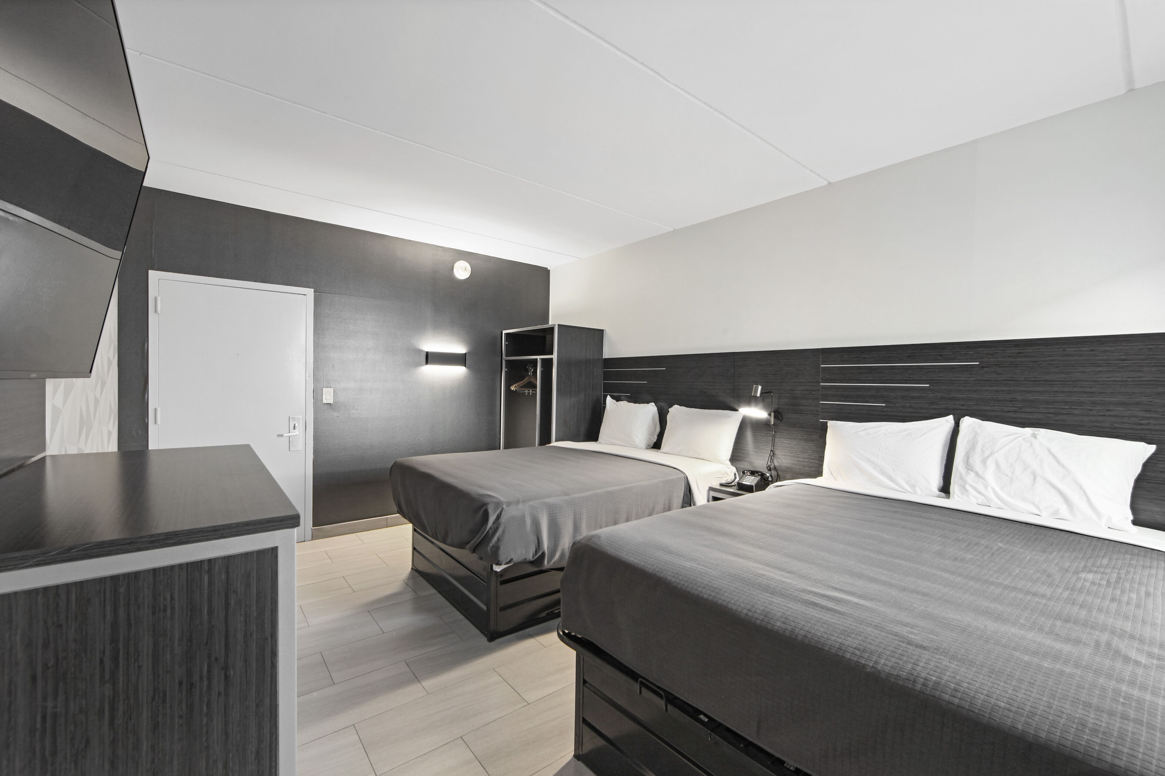 A modern hotel room with two beds, a wardrobe, and a desk.