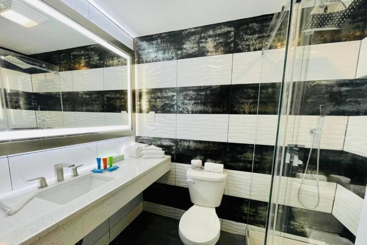 A modern bathroom with a large mirror, two sinks, a toilet, and a glass-enclosed shower.