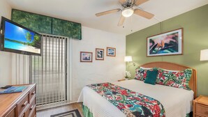A bedroom with a bed, a TV, a ceiling fan, and a window with a view of the beach. - Lea Casa at Casa de Emdeko (Kailua-Kona)