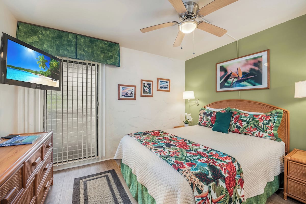 Un dormitorio con cama, televisión, ventilador de techo y ventana con vista a la playa.