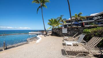 A poolside area with lounge chairs, a stone wall, and a view of the ocean.