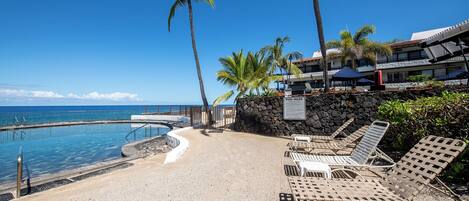 A poolside area with lounge chairs, a stone wall, and a view of the ocean.