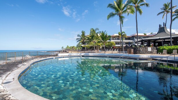 A clear pool with a stone pattern, surrounded by palm trees and a building with a distinctive roof. - Lea Casa at Casa de Emdeko (Kailua-Kona)