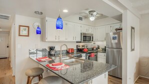 A modern kitchen with white cabinets, a granite countertop, stainless steel appliances, and pendant lighting. - Lea Casa at Casa de Emdeko (Kailua-Kona)