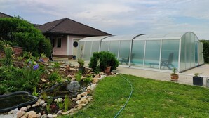 A greenhouse with a glass roof, a small pond, and a garden with various plants and rocks. - VACATION WITH DOG IN VACATION HOME WITH TERRACE GARDEN AND POOL (Stegersbach)