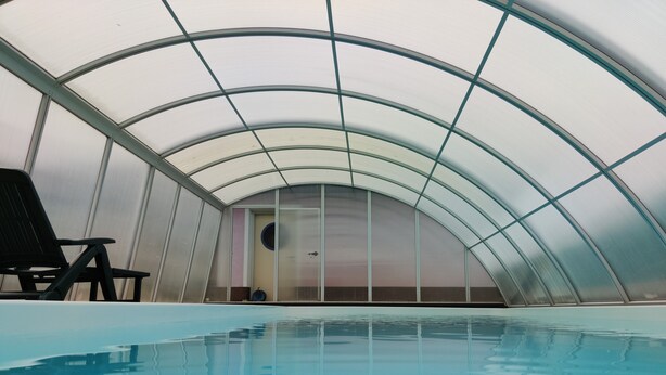 An indoor swimming pool with a glass ceiling, a door, and a black lounge chair. - VACATION WITH DOG IN VACATION HOME WITH TERRACE GARDEN AND POOL (Stegersbach)