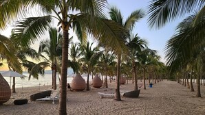 A beach with palm trees, lounge chairs, and woven seating areas.