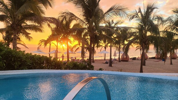 A swimming pool with a clear view of the beach and palm trees in the background.