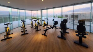 A modern gym with stationary bikes and a rowing machine, large windows offering a city view.
