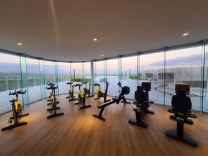 A modern gym with stationary bikes and a rowing machine, large windows offering a city view.