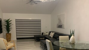 Un salon moderne avec une table à manger en verre, un ventilateur de plafond et un lustre.