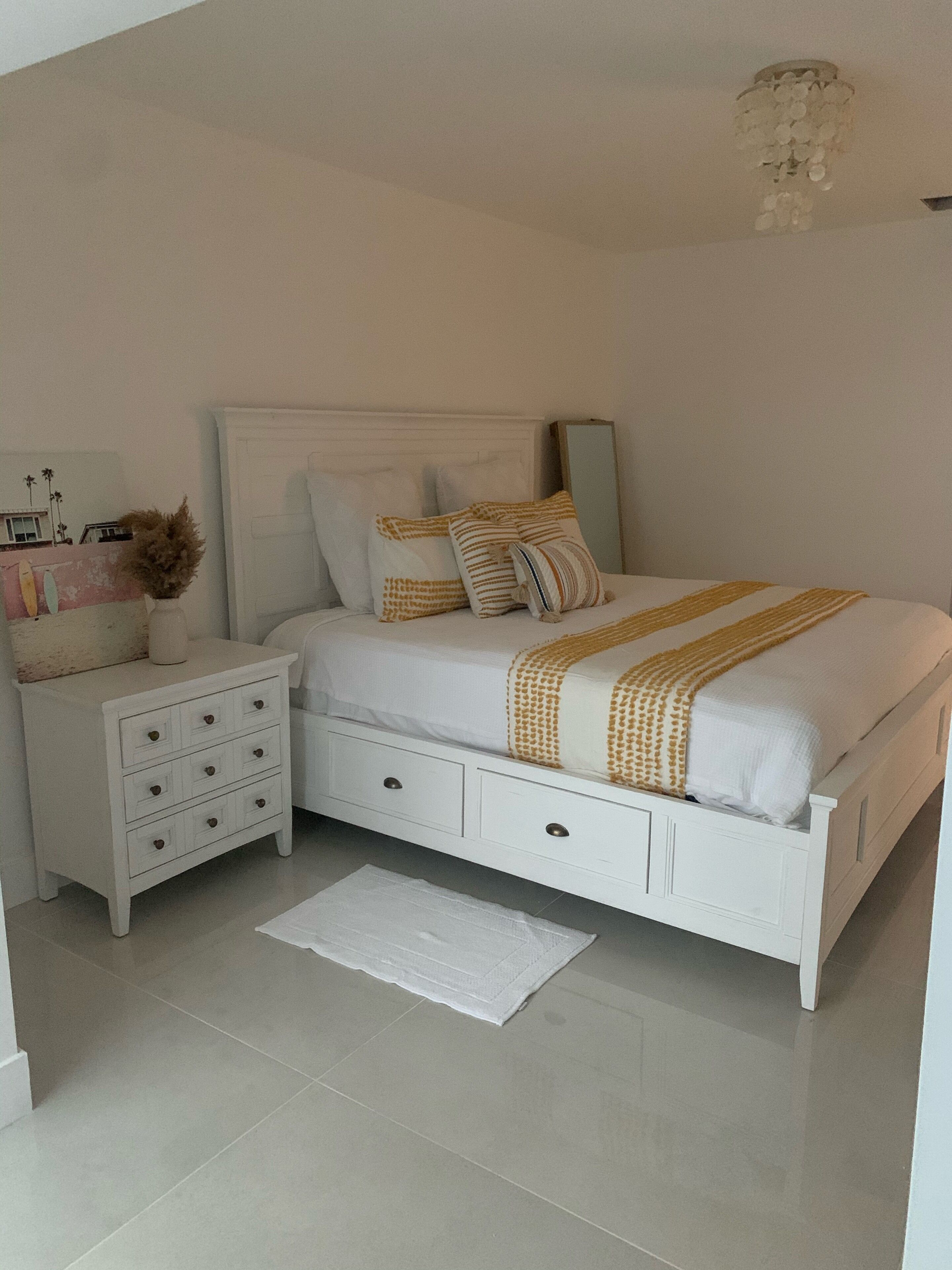 A bedroom with a white bed, a nightstand, a dresser, and a mirror.